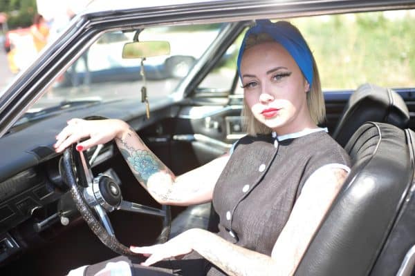 Vu de face de la mannequin qui porte le bandeau bleu qui se noue sur le devant elle est dans une voiture retro
