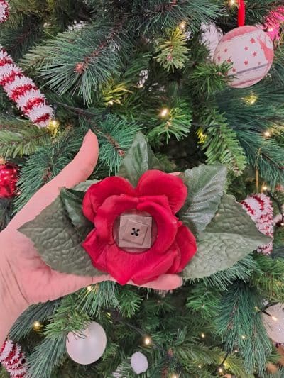 Pince à cheveux de couleur rouge avec en son centre un grand bouton en forme géometrique brun. Autour de la rose il y a des pétales vertes