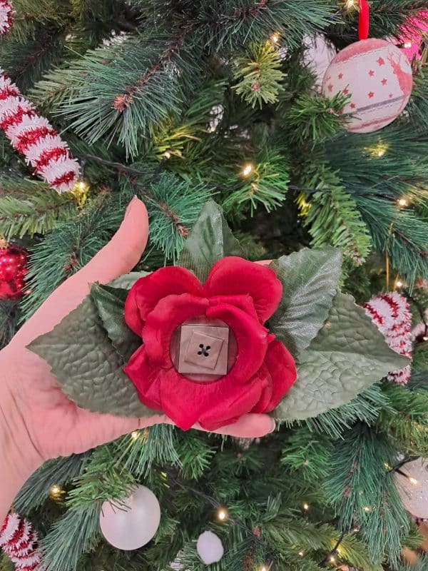 Pince à cheveux de couleur rouge avec en son centre un grand bouton en forme géometrique brun. Autour de la rose il y a des pétales vertes