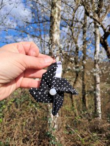 Porte clé avec de l'origami en forme de moulin de couleur noir à pois blanc dans un decor devant un arbre en fleurs