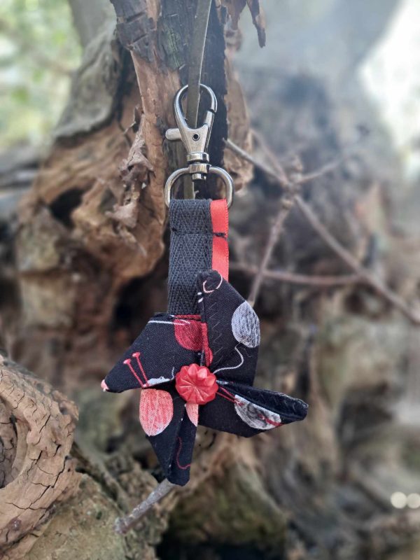 Porte cle en origami avec un motif de tricot noir et rouge presenter devant un element de la nature