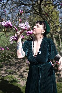 Dans un cadre de jardin une model retro porte un collier de perles noirs et fleur bleu