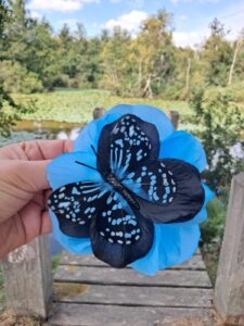 Pince à cheveux fleur bleue et noire avec papillon en plumes, 12 cm, tenue devant un étang
